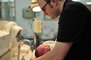 A man washing a baby&#039;s hair under the tap.