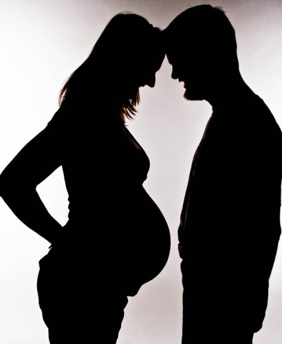 A pregnant womand and a man standing face to face looking and the woman's belly.