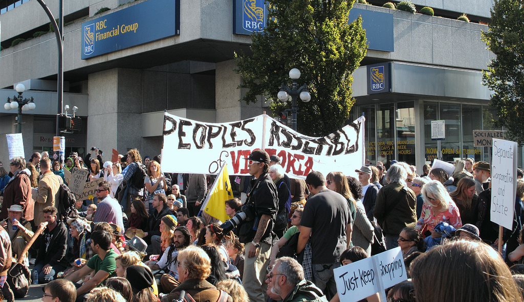 A large crowd of people gathered on the street. One sign says, &quot;Peoples Assembly of Victoria.&quot;