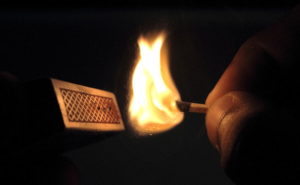 A burning match, held beside a matchbox.