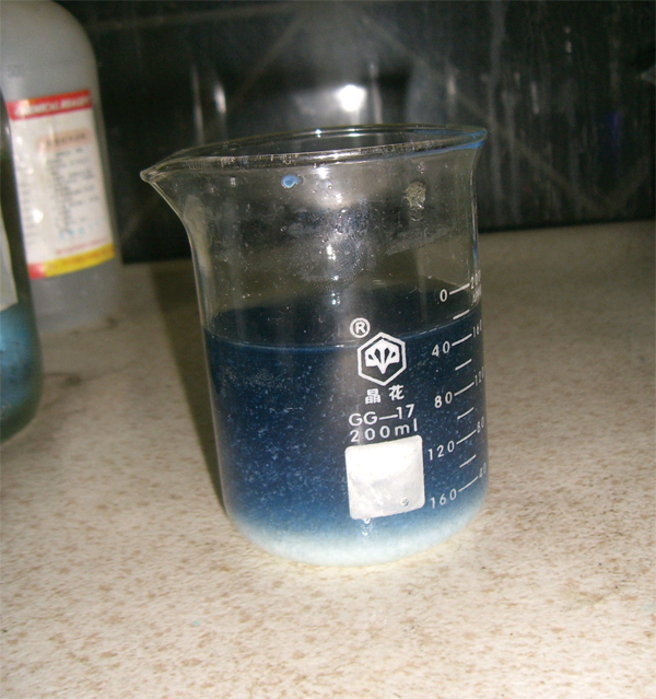A beaker full of a blue liquid. Some white solids are at the bottom.
