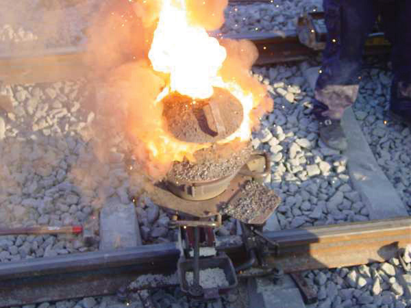 A clay pot with flames and smoke coming out of it sitting on railway tracks.