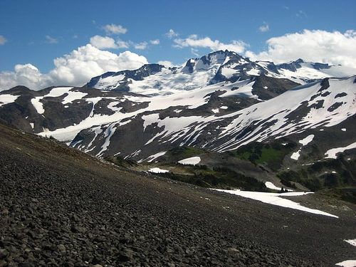 A large mouuntain with bare rock showing through the snow.
