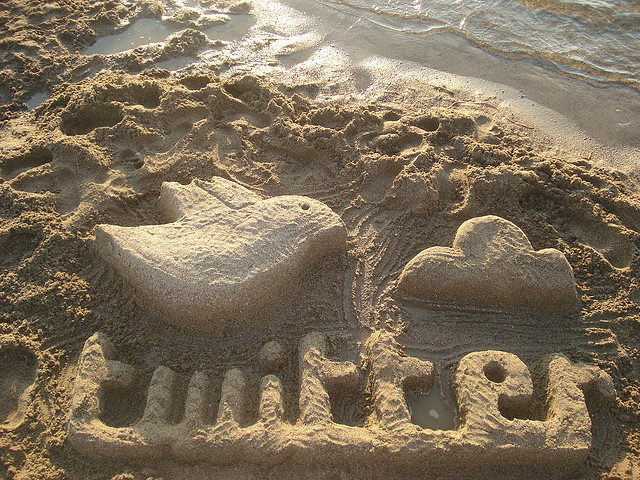 The twitter logo carved out in the sand.