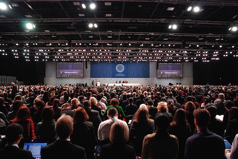 A large crowd of people sit in a lecture hall.