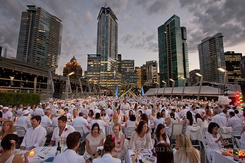 Rows of tables with people dressed fancily in white sitting around them.