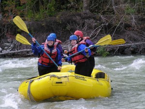 Four people kneel on a raft holding paddles and wearing helmets and lifejackets.