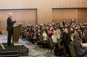 A man stands at a lecturn and speads to a crowd.