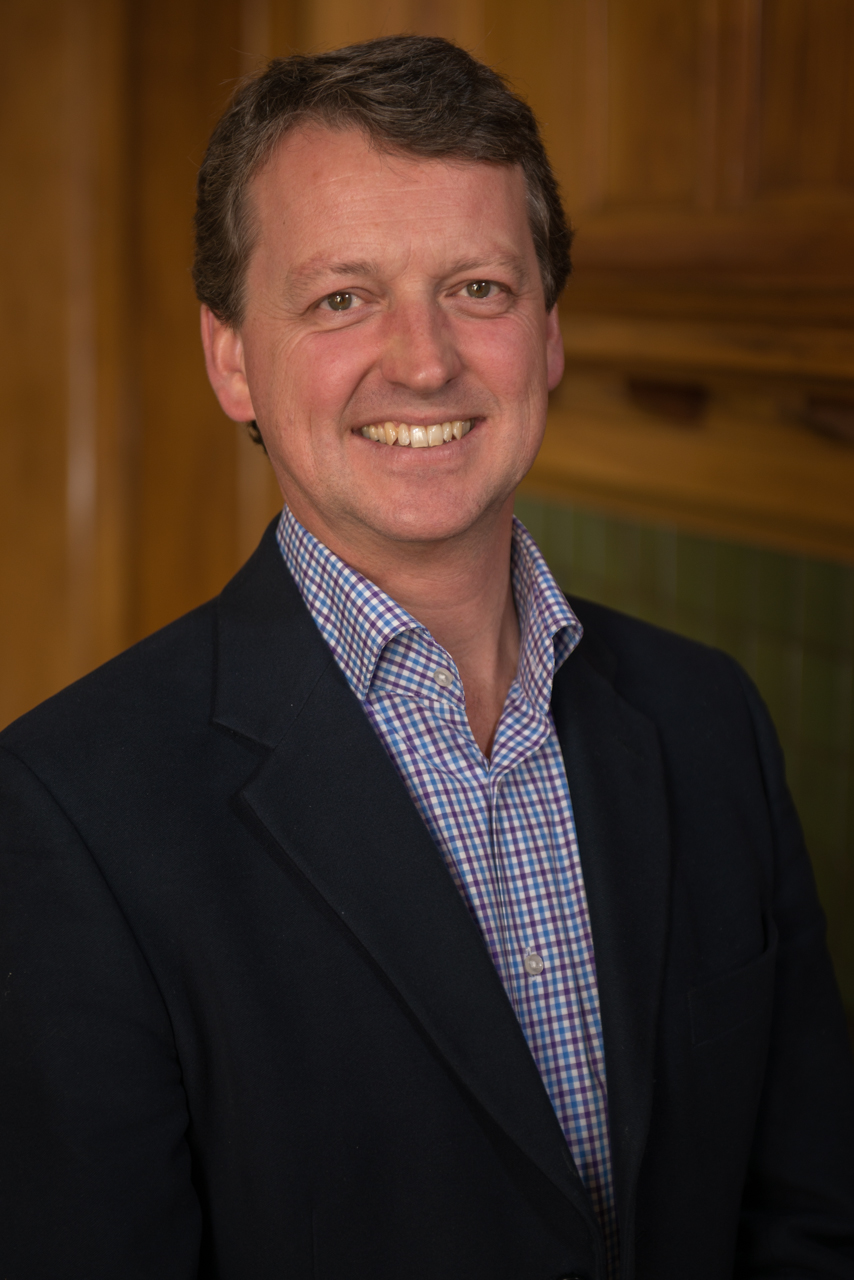 A smiling middle-aged man in a blazer and collared shirt.