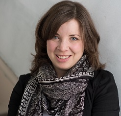 A young woman wearing a black patterned scarf smiles.