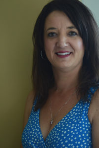 A woman wearing makeup and a blue sleeveless top with white polka dots smiles.