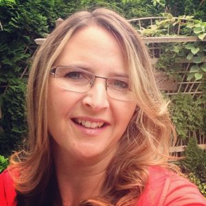 A selfie of a smiling middle-aged woman in front of a wooden trellis in a garden.