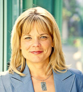 A blonde woman in a blazer poses outside.