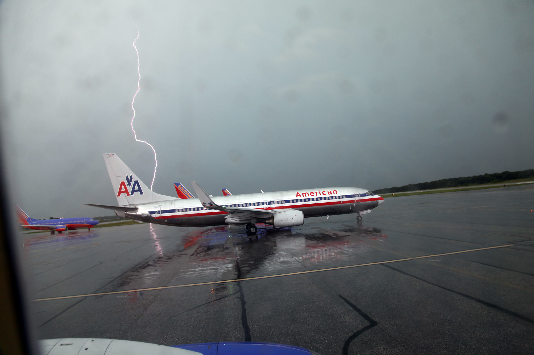 An airplane on a wet runway with lightning in the background.
