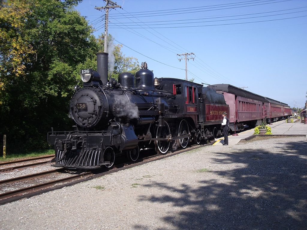 A black steam train pulls several cars beneath a blue sky.
