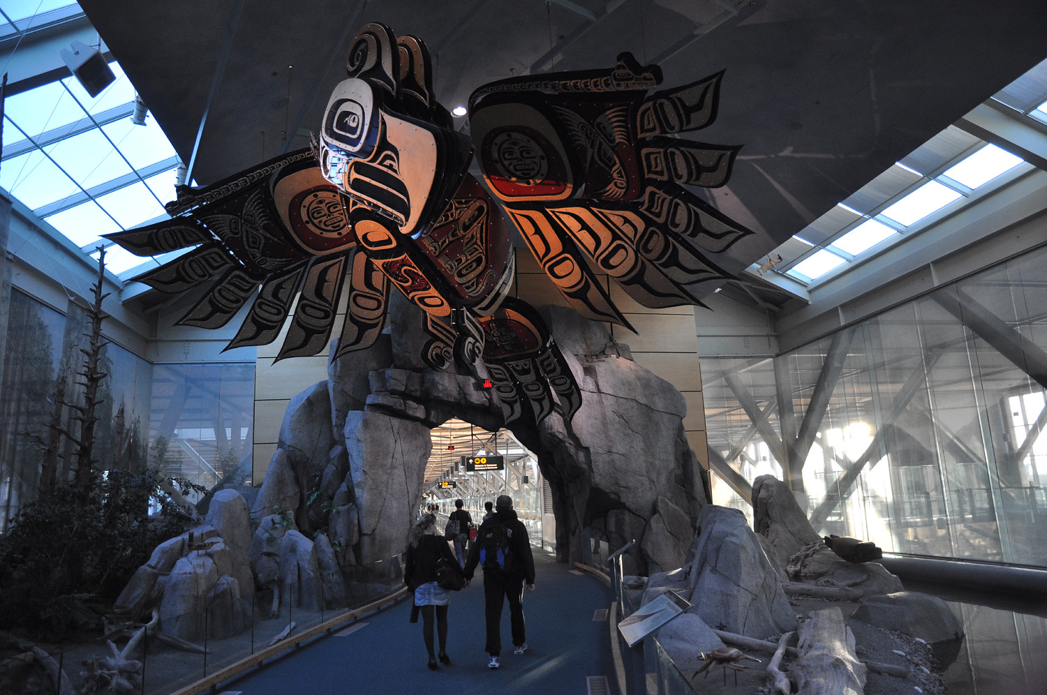 A huge carved bird painted in black and red hangs over an entryway in an airport.