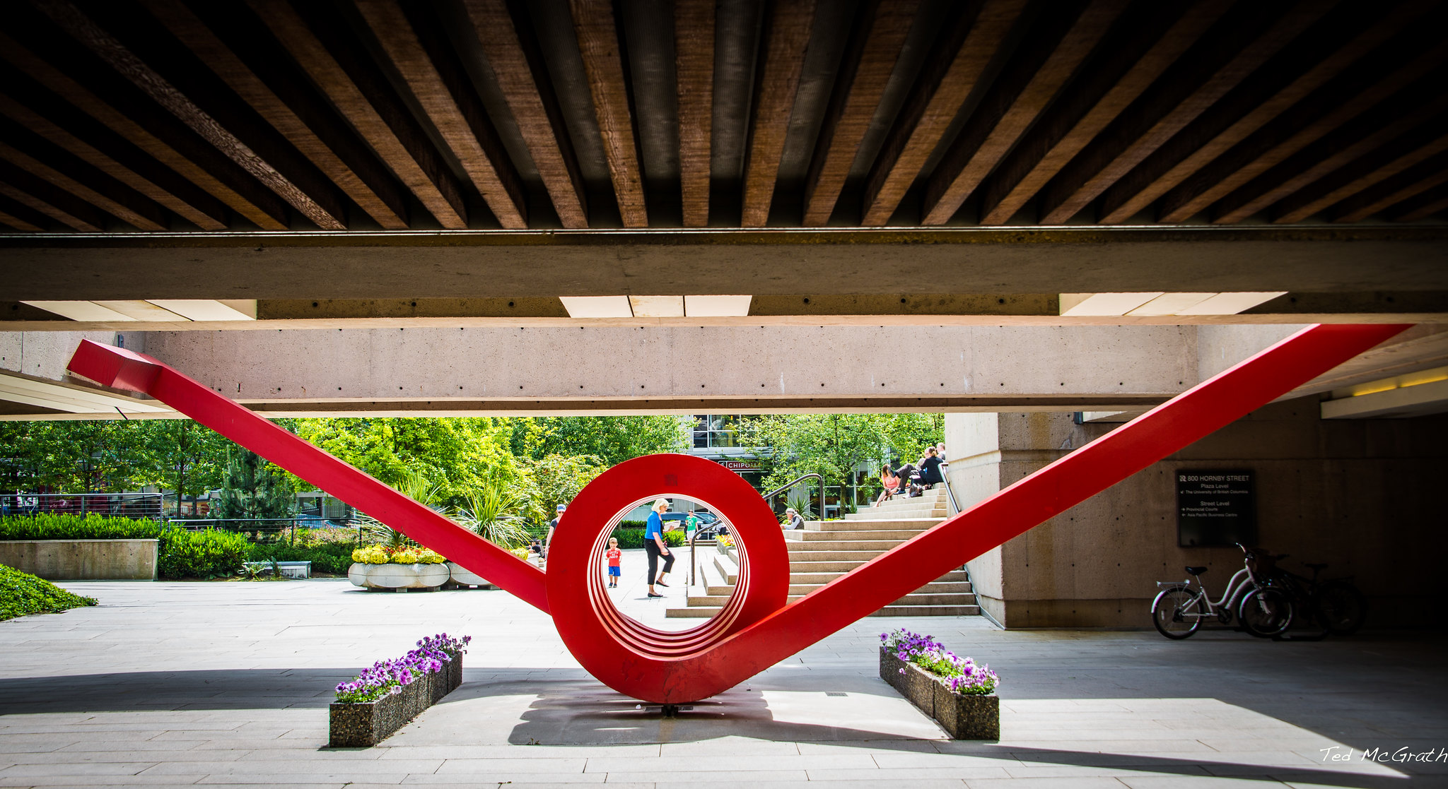 A red metal sculpture with a spring-like tunnel and two arms sticking out at wide angles.