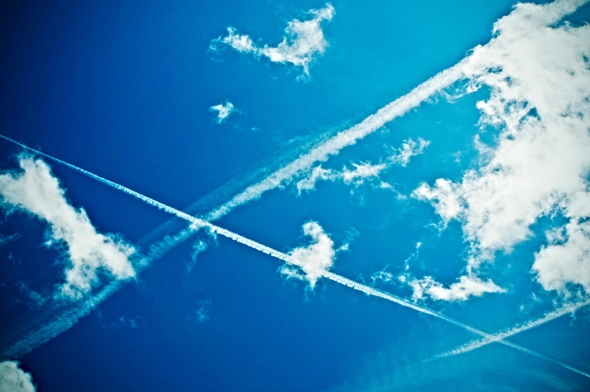 Plain contrails streak across a blue sky with a few clouds.