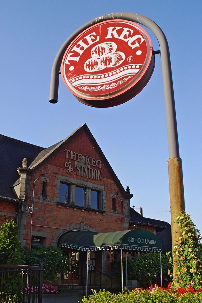 An old brick train station with a green entrance awning. A sign that says &quot;The Keg&quot; hangs on a pole.