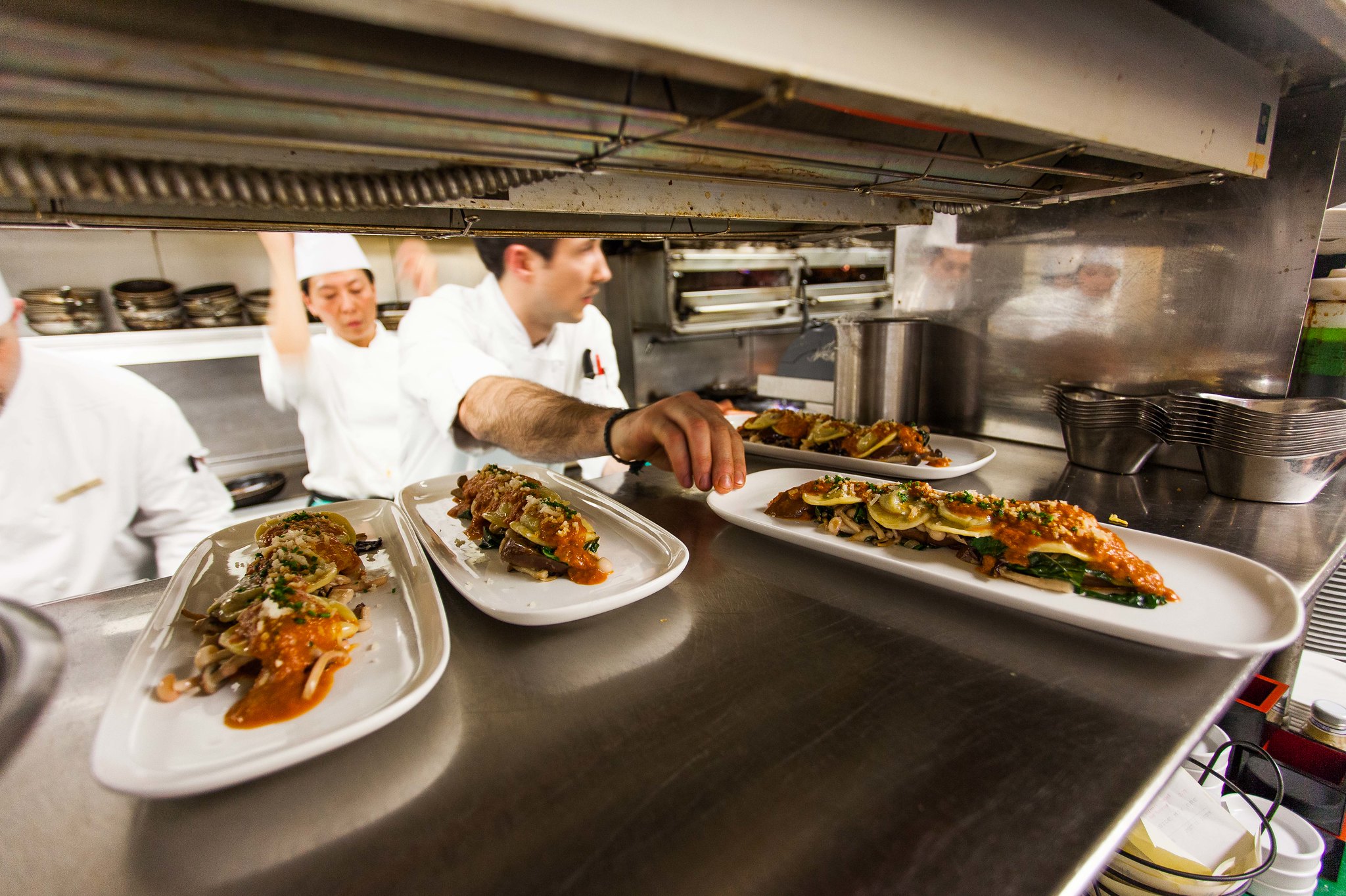 A chef sets plates of gourmet food onto the passthrough in a busy kitchen.