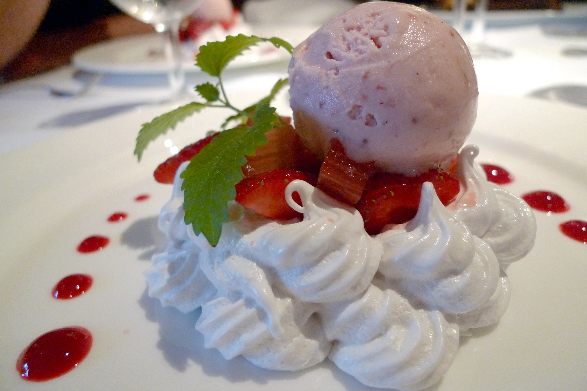 A dessert of pink ice cream served on top of strawberries, rhubarb, and meringue.