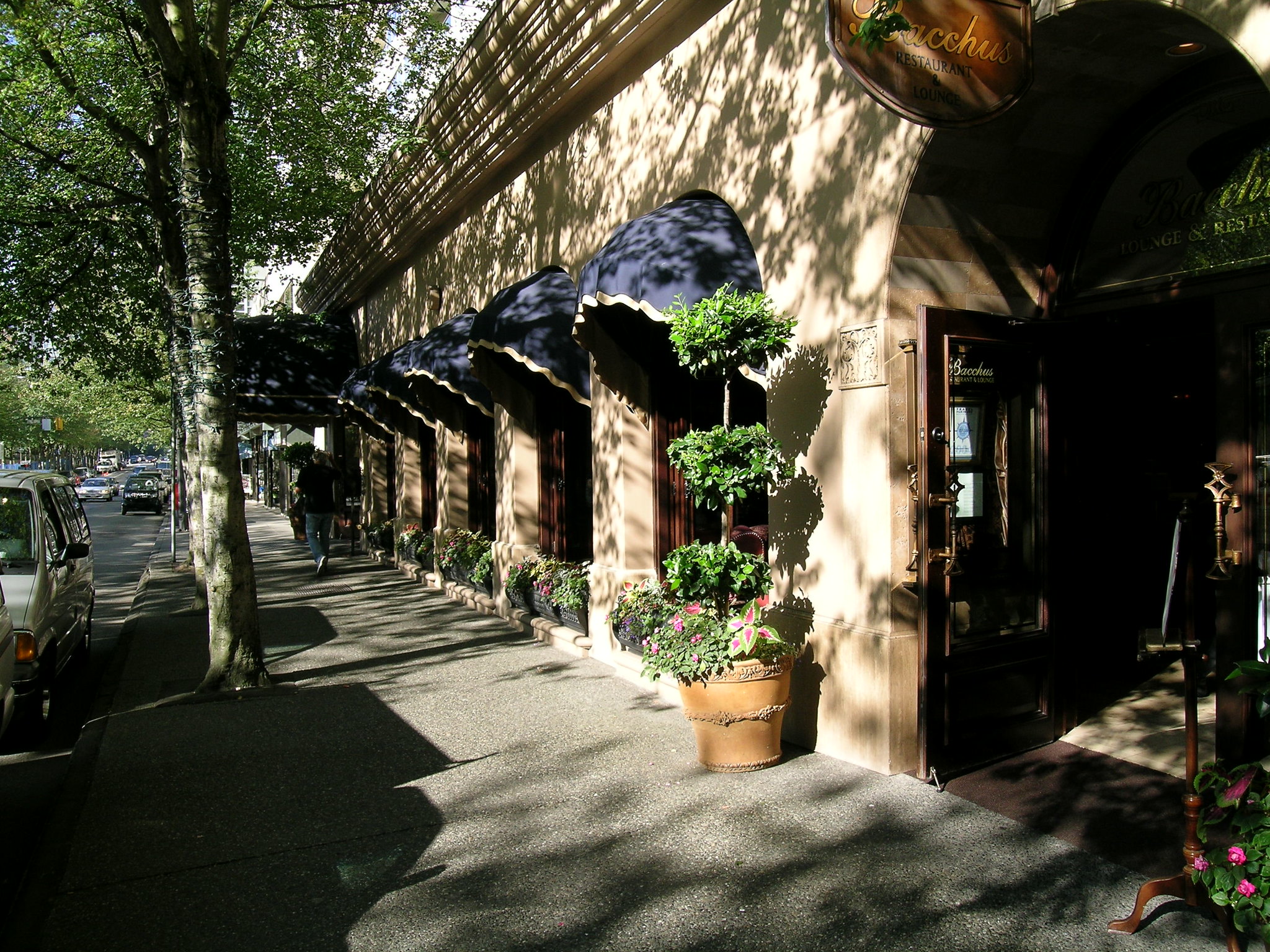 The entrance to a hotel restaurant called Bacchus, shaded by trees lining the street.