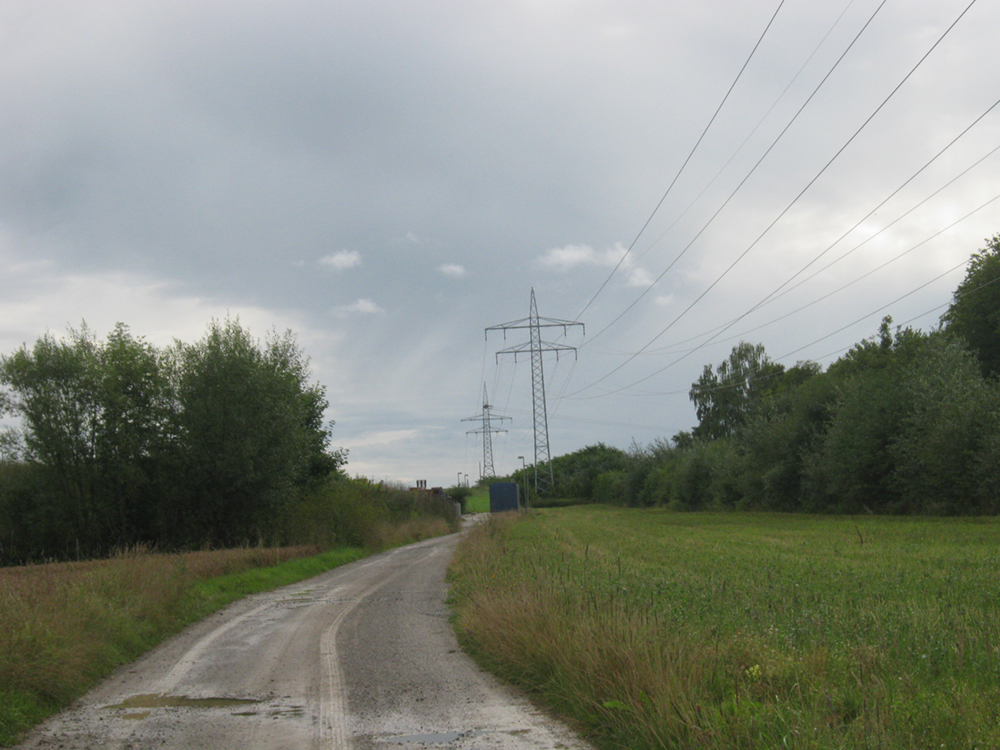 A high-voltage traction power line is shown to the side of a roadway. The power line in the photo has two transmission poles supporting the cables.