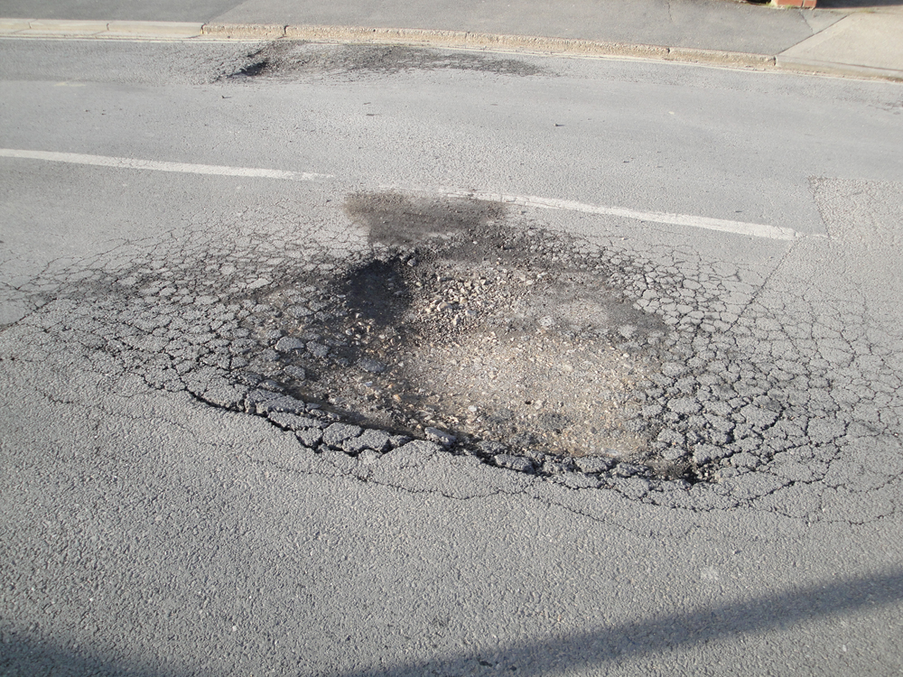 A cracked asphalt road with a pothole.