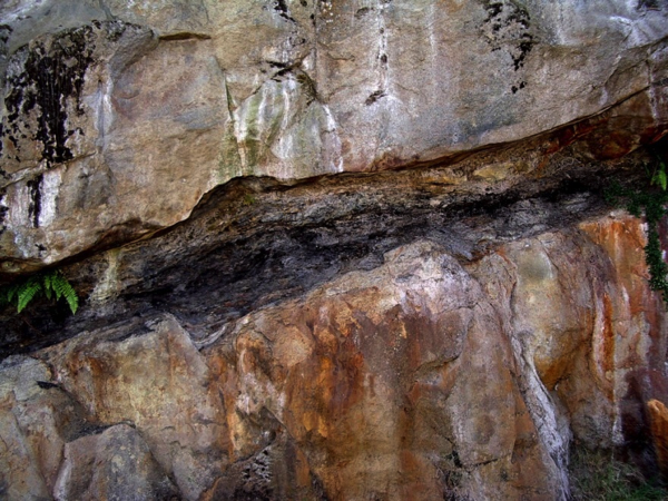 A tall, light coloured rock wall with a black streak running through the middle.