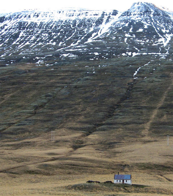 A steep slope has a wrinkled texture. A tiny abandoned farmhouse sits at the base.