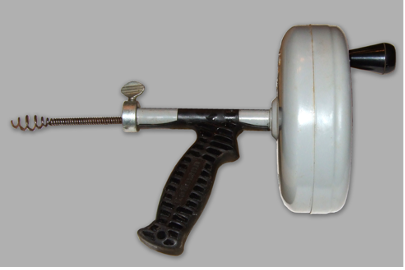 The drain auger has a large disk with a hand crank, a handle to hold it steady, and a wire cable with a spiral whisk-like shape at the end. The large disk houses the rest of the cable.