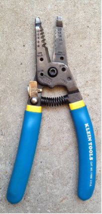 Plier-like device with a handle, pair of jaws, and a spring but with semicircular holes in both of the jaws. Each semicircle combines to create a circle that is sized to strip a certain size of wire. There are five sizes of wires that these wire strippers can strip.