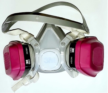 The respirator mask has a strap to go around the back of the head and the mask itself fits over the nose and mouth. Attached to the mask are two pink filters.