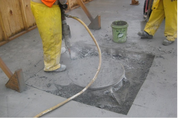 Workers are jackhammering the concrete around the manhole.