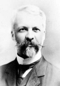 Photo portrait of an older man in a suit with a moustache and a goatee.