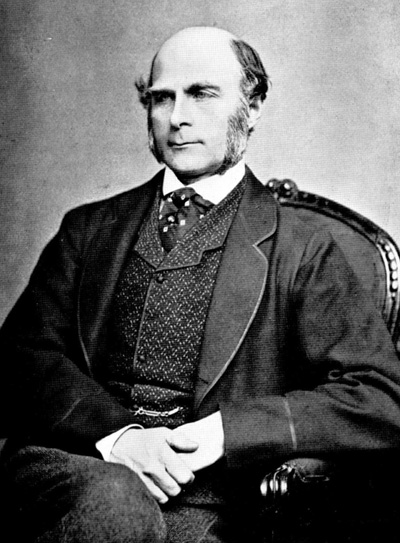 A man with mutton chops wears a suit and sits in an armchair.