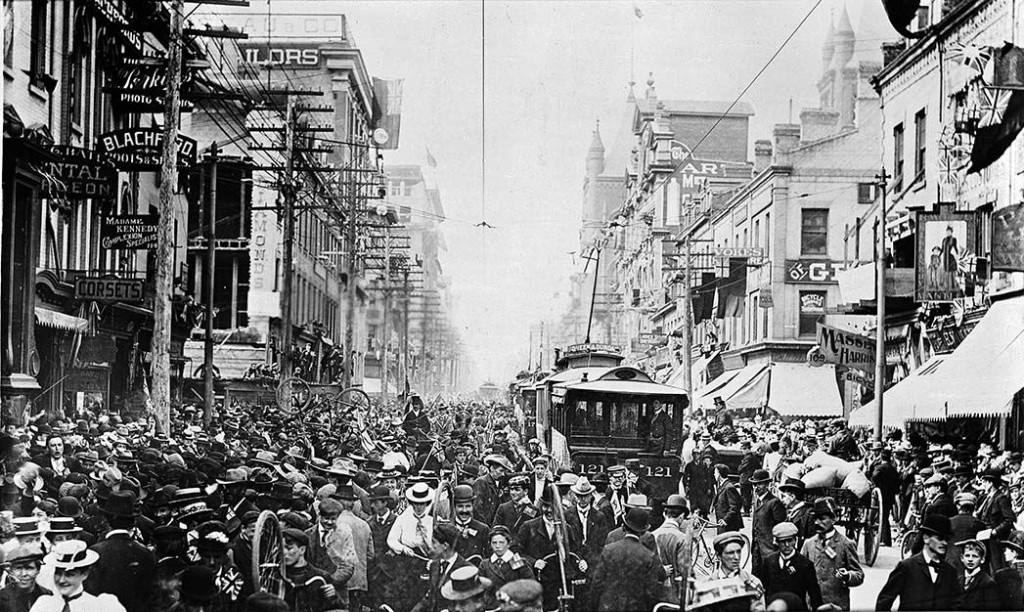 A packed city street with a street trolley surrounded by people.
