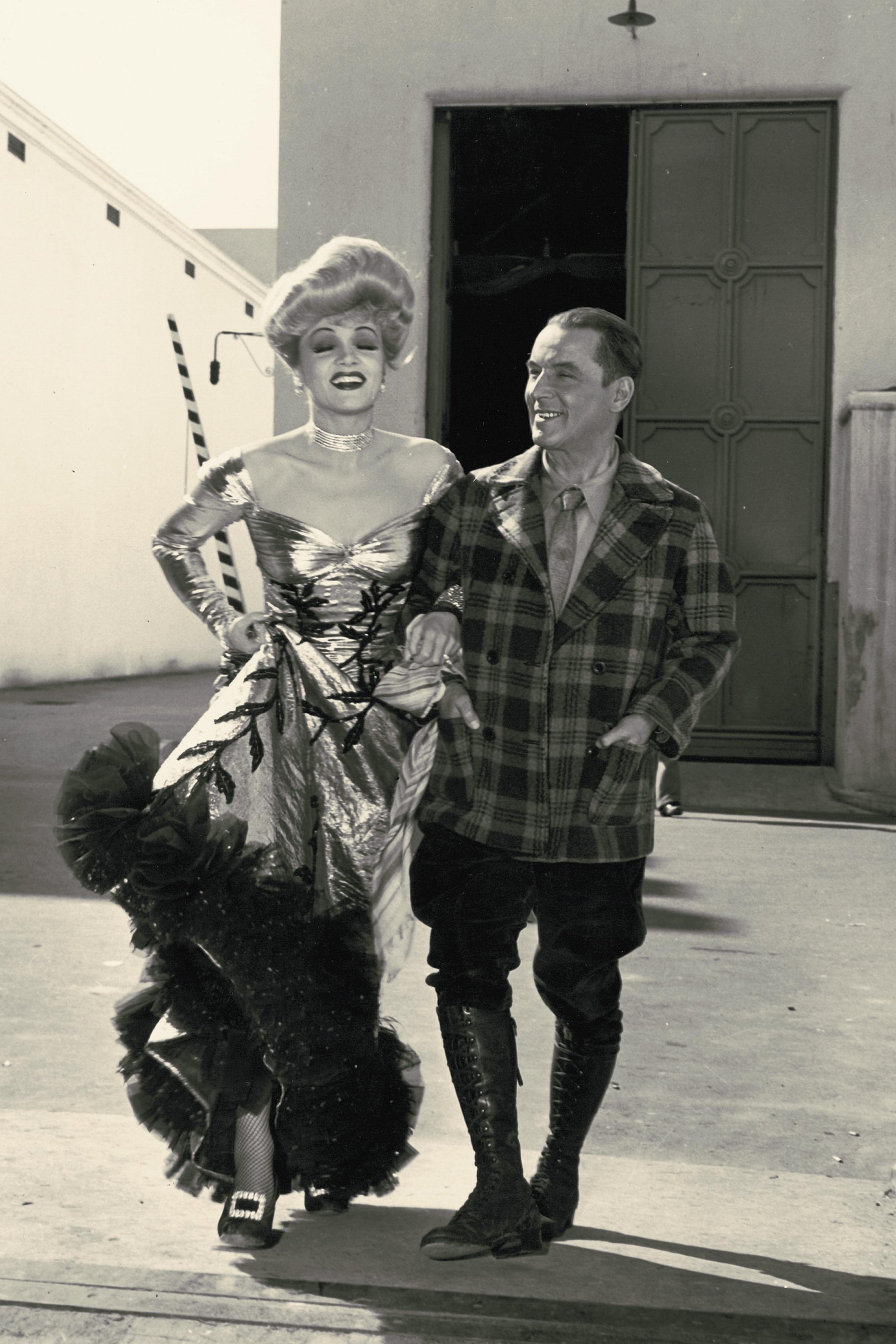 A man in a plaid blazer smiles at a woman in a glamorous dress.