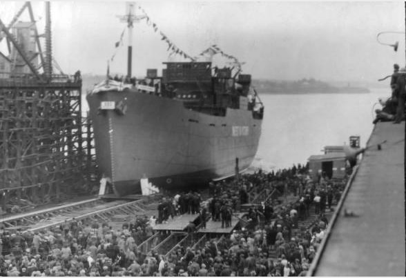 A large ship sits at a dock. Many people are gathered on the dock.