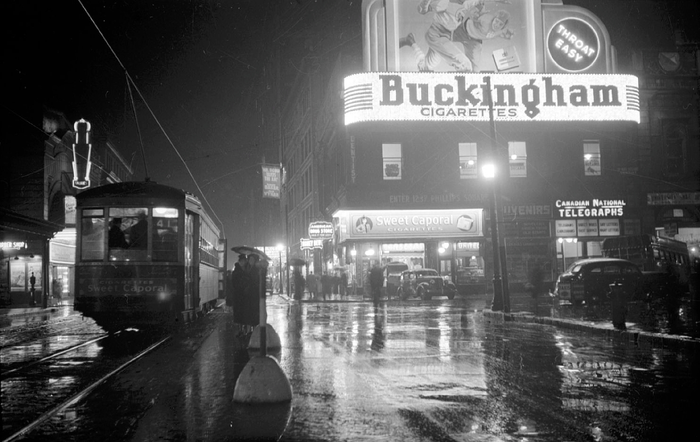 Nightscape. A streetcar passes a building with a neon sign advertising Buckingham cigarettes.