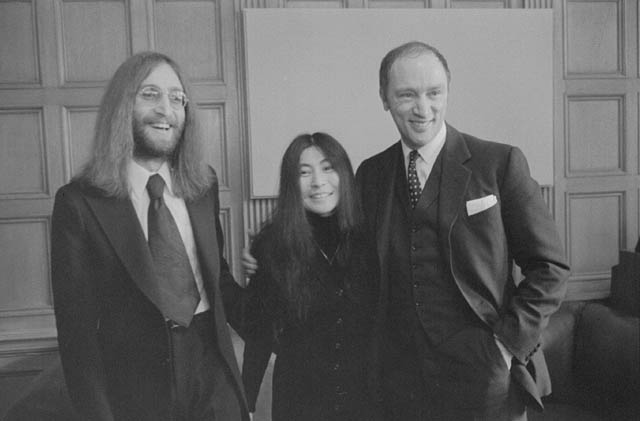 A man with long hair poses beside a Japanese woman. A man grins and has his arm around the woman.