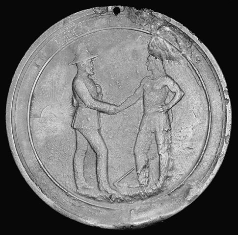 A medal showing a white man shaking hands with an Indigenous man wearing a headdress.