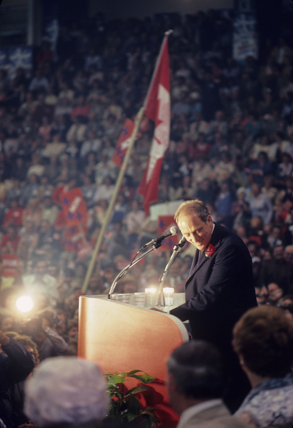 A man standing at a podium ducks his head, smiling. He speaks to a huge crowd.