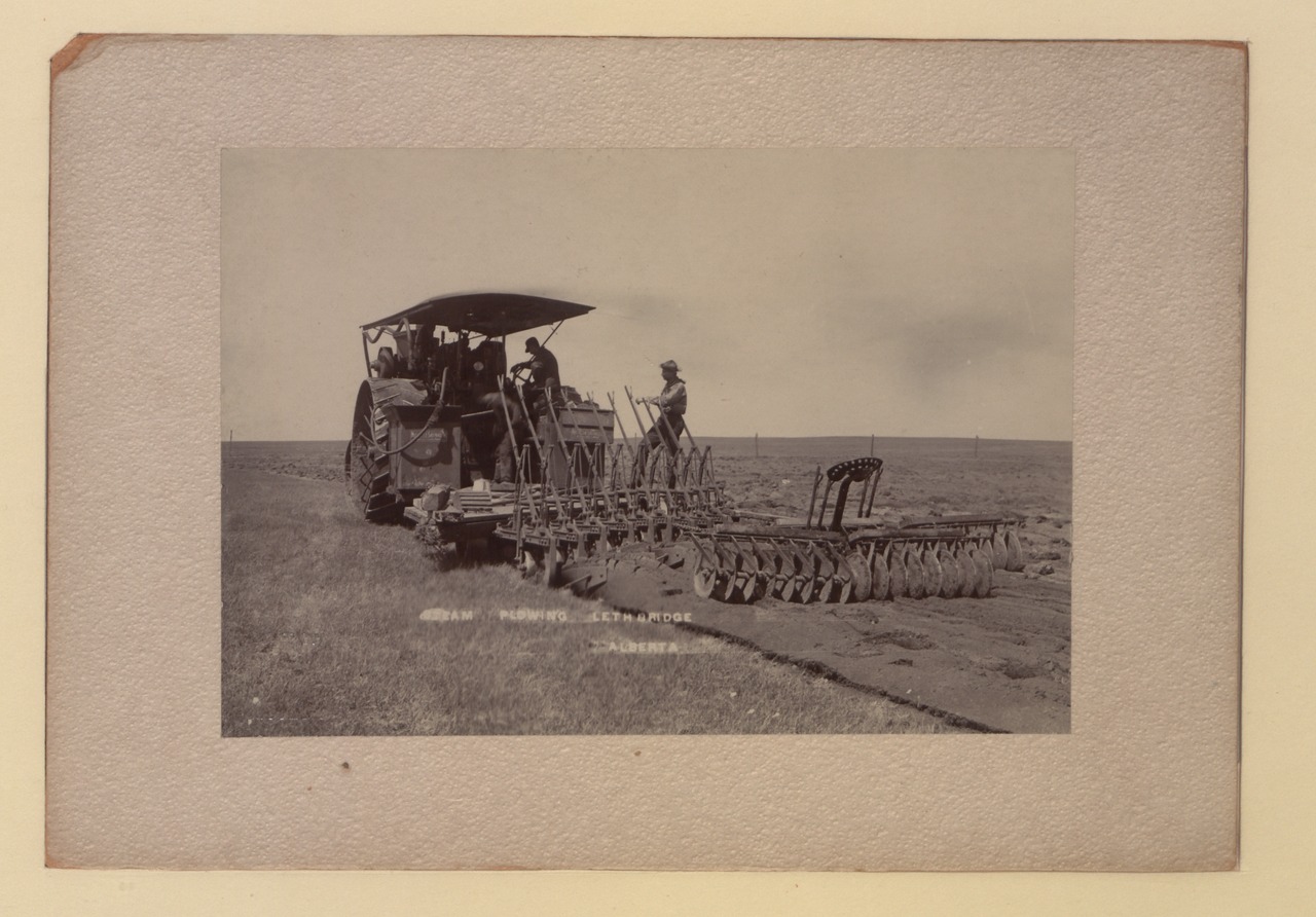 Two men operate a tractor on a field.