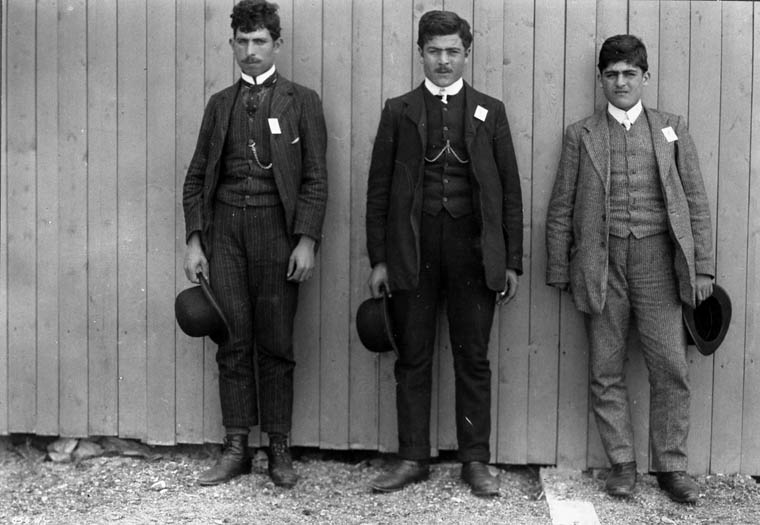Three young men with white squares pinned to their suits stand in a line.
