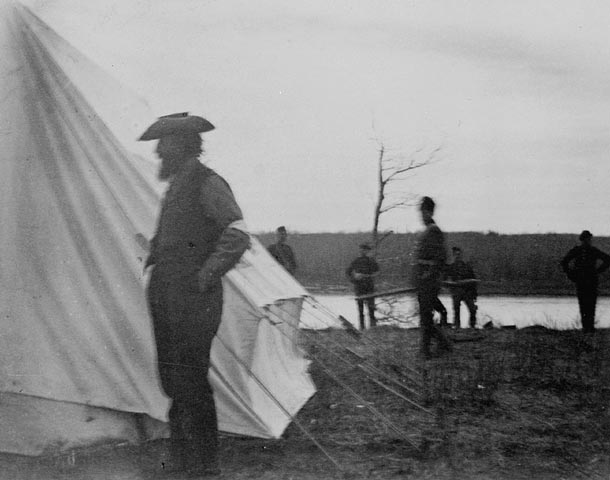 Riel standing in front of a tent by a river.