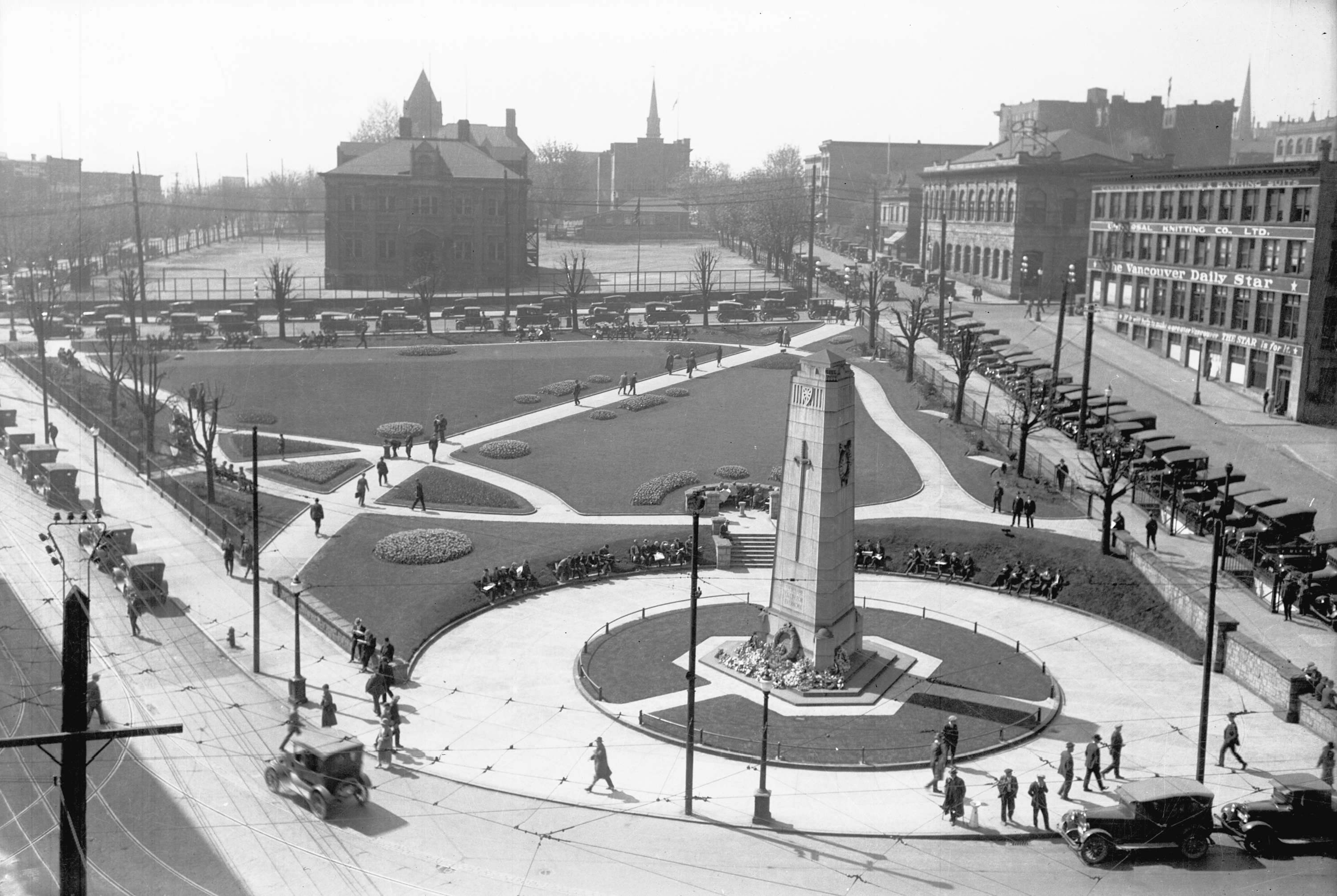 Rectangular stone memorial is the focus of a city square. Landscaping and buildings surround it.