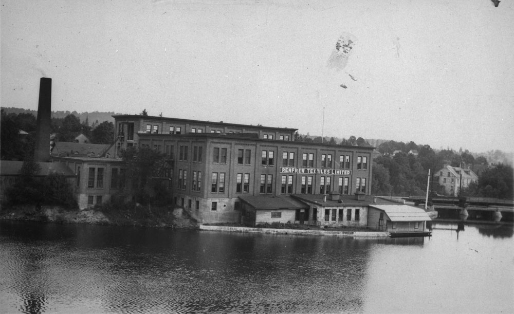 Brick factory with a smokestack on a riverbank.