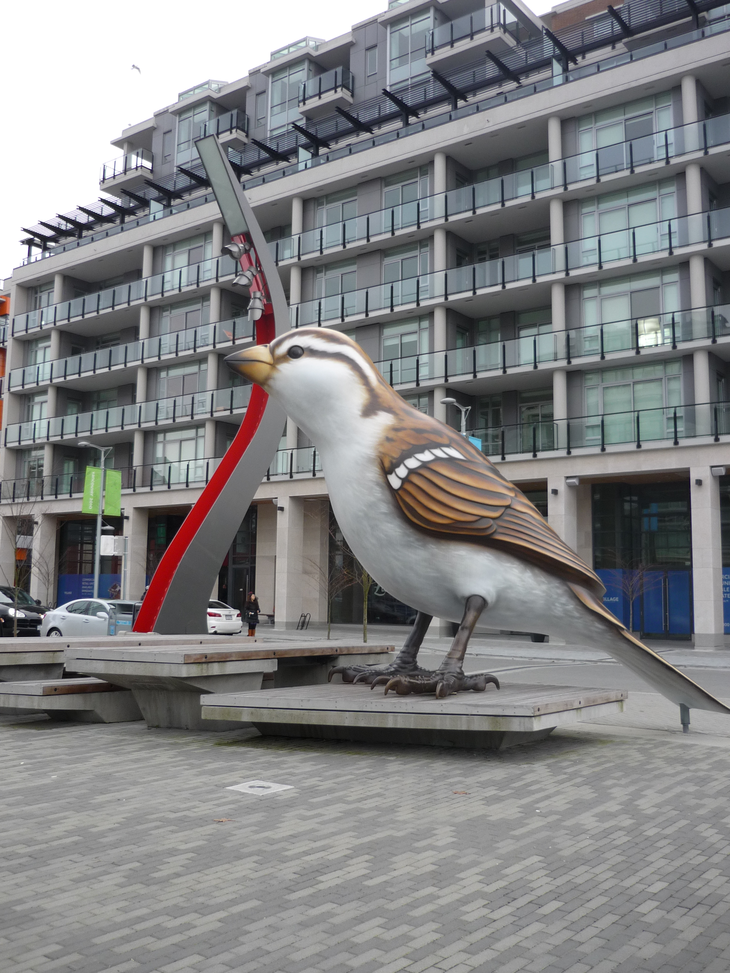 A giant statue of a sparrow stands outside a condo building.