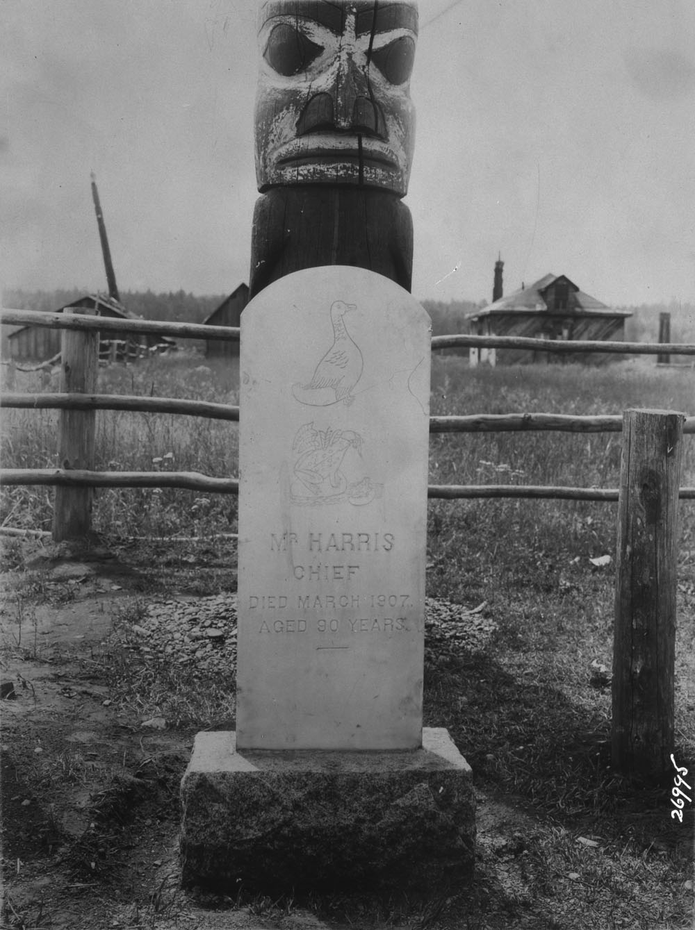 A tombstone in front of a totem pole. It says "Mr Harris Chief. Died March 1907, aged 90 years"